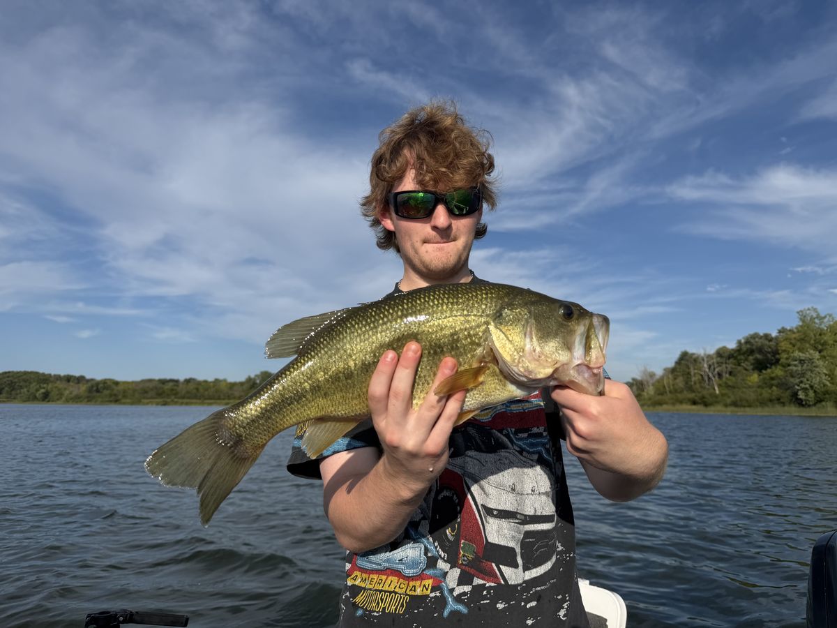 A young angler holding a largemouth bass in the boat